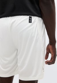 Λευκά αθλητικά σορτς από ελαφρύ ύφασμα, με πλευρική ραφή, ενθέσεις από δίχτυ και μια μικρή μαύρη ετικέτα με λογότυπο στη μέση.