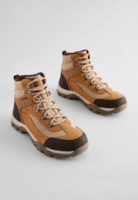 Brązowe i beżowe buty trekkingowe z wysokim fasonem, wykonane z teksturowanej skóry i materiałów syntetycznych, z metalowymi oczkami i solidnymi podeszwami.