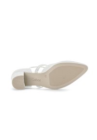Chaussure à talons scintillante blanche avec une semelle en caoutchouc texturé. Présente des brides croisées et un design à orteils pointus. Logo de la marque visible sur la semelle.