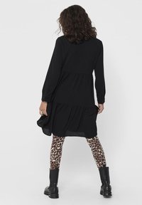 Abito nero a maniche lunghe con design a strati; indossato con leggings a stampa leopardata e stivali da combattimento neri. Tessuto morbido con vestibilità rilassata.
