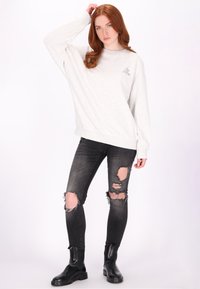 Lichtgrijze sweatshirt met een losse pasvorm en lange mouwen, gecombineerd met versleten zwarte jeans met opvallende scheuren. Zwarte enkellaarsjes.
