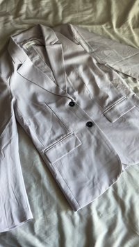 Blazer gris claro hecho de tela suave, con dos bolsillos frontales, dos botones negros y un diseño de solapa muesca.
