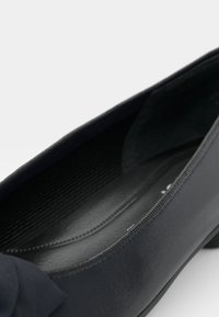 Ballerine noire avec un extérieur en cuir lisse, bout arrondi, détail de nœud discret à l'avant et doublure intérieure texturée.