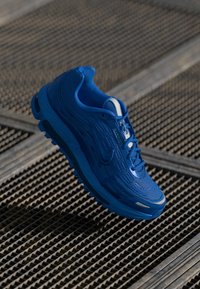 Blue athletic shoe with textured mesh upper and supportive sole. Features contrasting white accents and a cushioned collar.