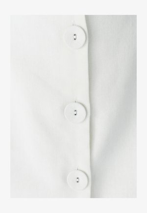 Witte button-up shirt met vier grote, ronde knopen, gemaakt van een gestructureerde stof en met zichtbare stiksels langs de sluiting.