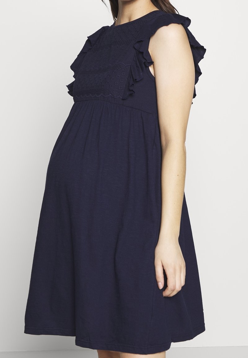 Mörkblå gravidklänning i mjukt tyg med volangkant vid halsringningen och detaljer vid bysten, med en flödande A-linjeform och ärmlös design.