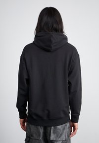 Sweatshirt à capuche noir avec une coupe décontractée. Comprend une grande capuche, des poignets et un ourlet côtelés. Fabriqué en tissu en coton doux, design minimaliste.