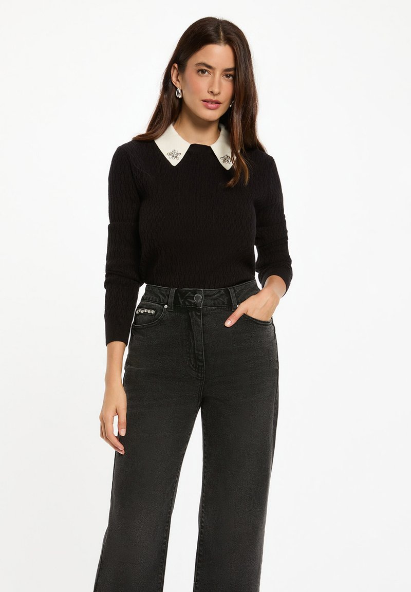 Suéter negro de canalé con un cuello blanco adornado con acentos decorativos, combinado con jeans oscuros de tiro alto.