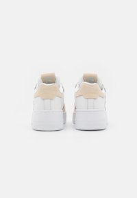 Hvite sneakers med beige detaljer, teksturert hæl og glatt tå. Har en polstret krage og preget logo detalj på hælen.