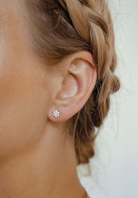 Pendiente de botón en forma de flor con múltiples pequeñas piedras preciosas transparentes incrustadas en una base de oro, llevado en la oreja de una persona. Detalles finos realzan el diseño.