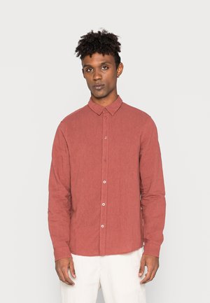 Long-sleeve button-up shirt in rusty red linen fabric, featuring a pointed collar and white buttons, textured surface, and straight hem.