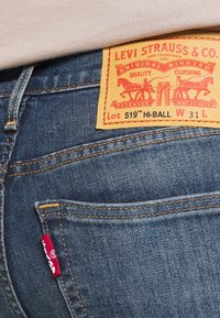 Bolsillo trasero de unos vaqueros Levi's azul con etiqueta de cuero marrón que muestra la marca, lote 519 Hi-Ball, talla 31, y una etiqueta de tela roja.