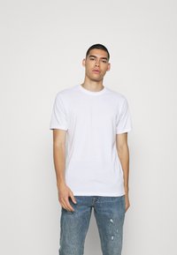 Weißes Kurzarm-T-Shirt aus glattem Stoff, mit rundem Halsausschnitt und geradem Schnitt, kombiniert mit blauen, verwaschenen Jeans.