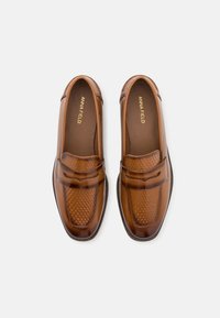 Brune skinnloafers med teksturert panel, glatt overdel og subtil søm. Merket "ANNA FIELD" på innersålen.