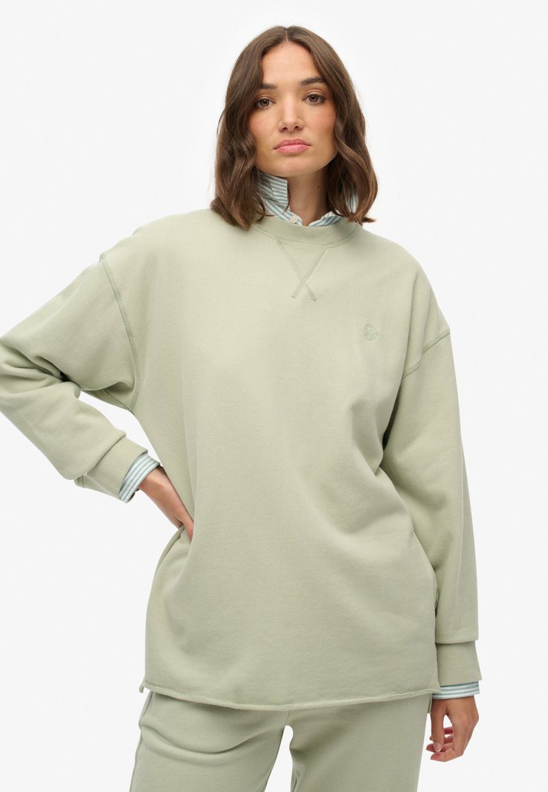 Sweatshirt troppo grande di colore verde chiaro con scollatura rotonda e polsini a coste, caratterizzato da un piccolo logo ricamato sul petto.