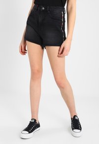 Mustat farkkushortsit, joissa on korkeavyötärö, revitty helma ja moniväriset raidat sivuilla. Yhdistetty mustiin tennareihin kontrastiksi.