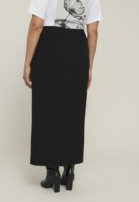 Fustă neagră, până la gleznă, cu o textură netedă și o siluetă ajustată. Asortată cu cizme negre cu toc până la gleznă.