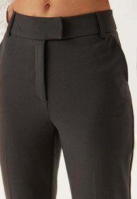 Op maat gemaakte donkergrijze broek met een gladde textuur, een middelhoge tailleband, centrale vouw en subtiele zijzakken. Voorflat ontwerp.