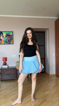 Gonna svasata azzurro chiaro con cintura elastica, abbinata a un top nero senza maniche. Pavimento in legno e opere d'arte colorate sullo sfondo.