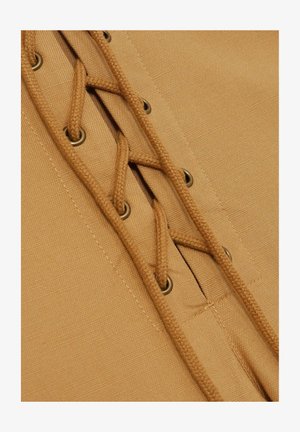 Design con lacci che presenta un tessuto beige con una trama intrecciata, occhielli con finitura metallica e lacci intrecciati che attraversano le aperture.