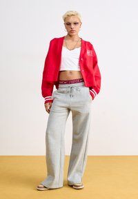 Red cropped cardigan with white stripes, white tank top, gray wide-leg sweatpants with Nike logo, and light brown sneakers.
