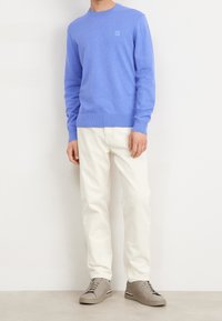 Pull bleu clair à col rond avec poignets côtelés, associé à un pantalon couleur crème et des baskets grises neutres. Éléments de design simples.