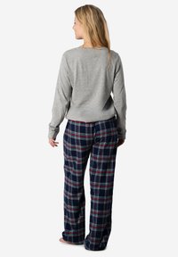 Grijze lange mouw top gecombineerd met marineblauwe geruite broek met rode en groene lijnen. Zachte stof, ontspannen pasvorm en ontwerp met volle lengte.