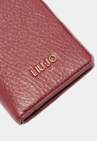 Portofel texturat de culoare bordo, cu un model embosat subtil, având un logo metalic auriu "LIU•JO" pe partea din față. Marginile netede completează designul.
