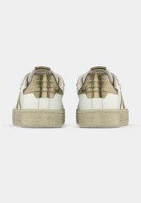 Weiße und goldene Sneaker mit strukturierten Fersenelementen, Obermaterial aus weichem Stoff und Gummiaußensohle. Sie zeichnen sich durch eine glatte Form und ein minimalistisches Design aus.