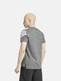 Camiseta atlética gris de manga corta con acentos a rayas en los hombros, un tejido texturizado y hendiduras en los lados para mayor movilidad.