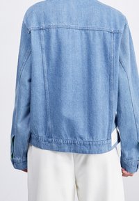 Light blue denim jacket featuring a relaxed fit, dropped shoulders, and side slit accents. Smooth texture with minimal stitching details.