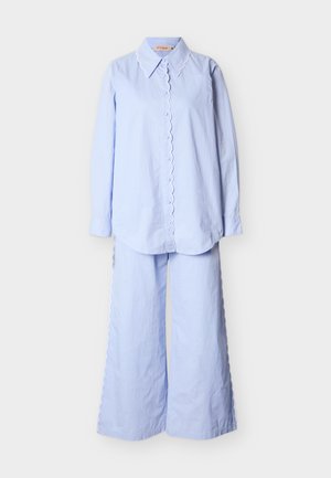 Φωτεινό γαλάζιο πουκάμισο μακρυμάνικο με κουμπιά και κυματιστά τελειώματα, συνδυασμένο με παντελόνι φαρδύ στο πόδι με κυματιστές λεπτομέρειες στο πλάι.