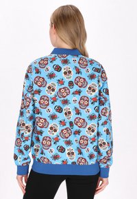 Hanorac albastru cu un model de cranii de zahăr colorate și flori, cu manșete și talie ribbate. Material fin și ușor.