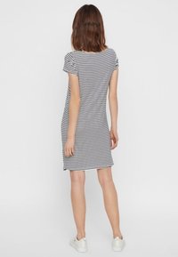 Czarna i biała w paski sukienka o krótkim rękawie, do kolan, z miękkiego materiału, dopasowany kształt, okrągły dekolt, noszone białe sportowe buty.