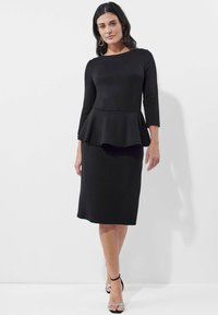 Schwarzes Plisseekleid mit langen Ärmeln und einem Bootsausschnitt, das einen taillierten Oberteil und einen knielangen Rock hat, aus glattem, dehnbarem Stoff gefertigt.