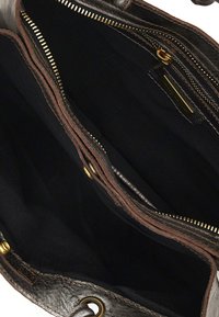 Interno di una borsa in pelle marrone con rivestimento in tessuto nero. Presenta più scomparti, zip in tonalità oro e dettagli di cucitura marrone.