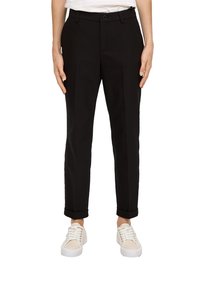 Pantalons noirs sur mesure avec une coupe droite, dotés de plis avant et de revers, fabriqués dans un tissu doux, associés à des baskets blanches.