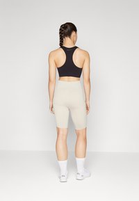 Juoda sportinė liemenėlė ir smėlio spalvos dviratininko šortai. Lygus audinys, prigludusi forma ir kelnės iki kelio. Modelis matomas iš nugaros. Baltos kojinės ir batai.