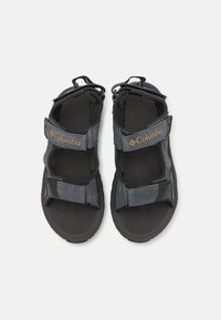 Mustakirjaga välisandlid Velcro rihmadega, pehmendusega jalatse ja tekstuuriga kummitald. Ülemisel rihmal on Columbia bränding.