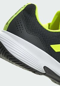 Czarno-limonkowe buty sportowe z teksturowaną siateczką u góry, wyściełanym kołnierzem oraz białą podeszwą z rowkowanym wzorem dla lepszej przyczepności.
