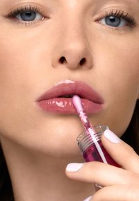 Applicatore per gloss labbra con liquido rosa, applicato su labbra piene. Finitura lucida con una sfumatura rosa tenue. Contenitore trasparente con applicatore a spugna.