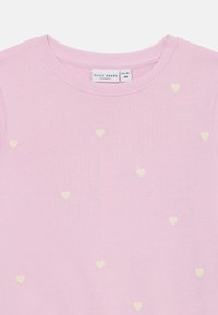 Sweatshirt rose clair en tissu doux, ornée de petits motifs en forme de cœur crème sur toute sa surface. Design à col rond avec bordure côtelée.
