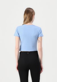 Tricou scurt, cu mânecă scurtă, de culoare albastru deschis, cu o textură moale și guler rotund, asortat cu pantaloni negri cu talie înaltă.