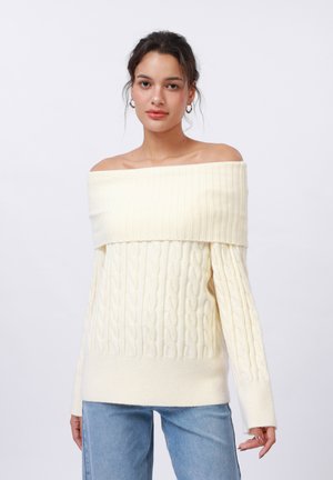 Crème off-shoulder trui met een ribbeltextuur en kabelbreisel, gecombineerd met lichtgewassen denim jeans.
