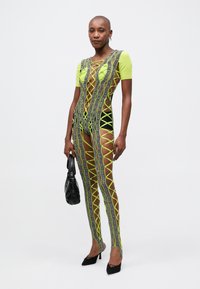 Neon zielony bodysuit z czarnymi akcentami, z krzyżującym się wzorem, krótkimi rękawami i wycięciami. Uzupełniony czarną torbą.