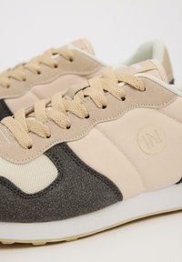 Zapatillas retro en tonos beige y gris con parte superior de tela, acentos texturizados y cordones planos beige. Cuenta con un logotipo circular en el lateral.