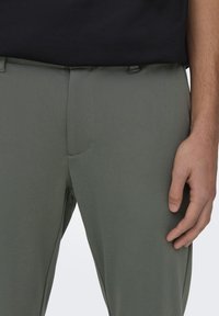 Pantalones verde oliva con una textura suave, diseño ajustado y detalles de costura sutiles en la cinturilla y la zona de los bolsillos.