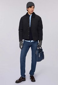 Černá prošívaná bunda, světle modrá košile pod tmavě modrým svetrem, modré džíny, šedá čepice, šedé rukavice a hnědé boty s modrou taškou.