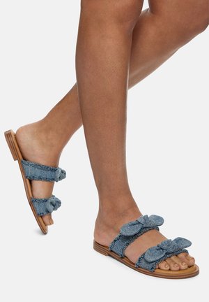 Sandales à glissière en denim avec deux grands nœuds en tissu sur les sangles, une semelle plate en tan et un design ouvert à l'avant.