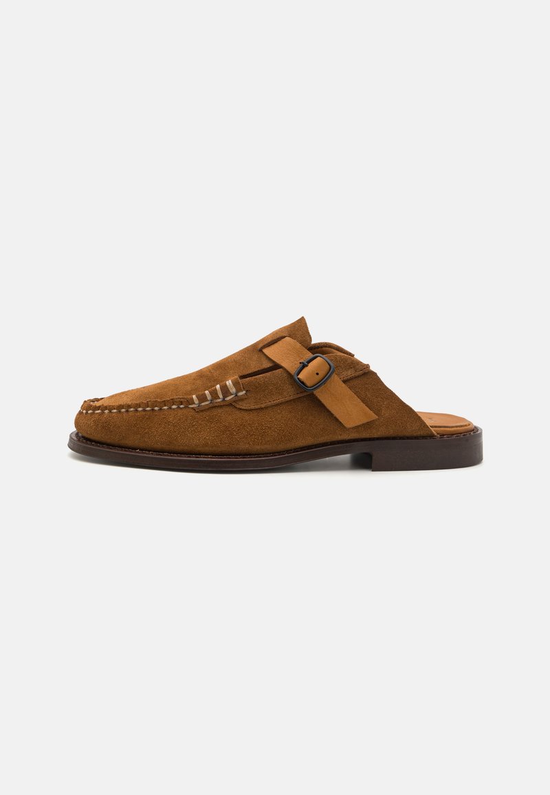 Scarpe slip-on in suede marrone con un design cucito, una tracolla decorativa con doppia fibbia e una suola marrone scuro.